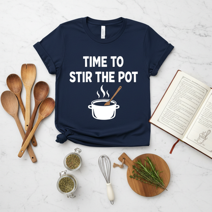 Overhead flat lay of folded time to stir the pot t-shirt with cooking spoons and recipe book